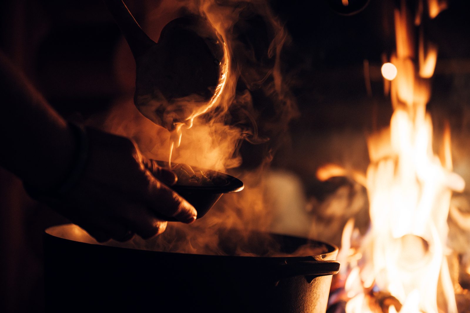 A ladle lifted steaming from the pot over the fire