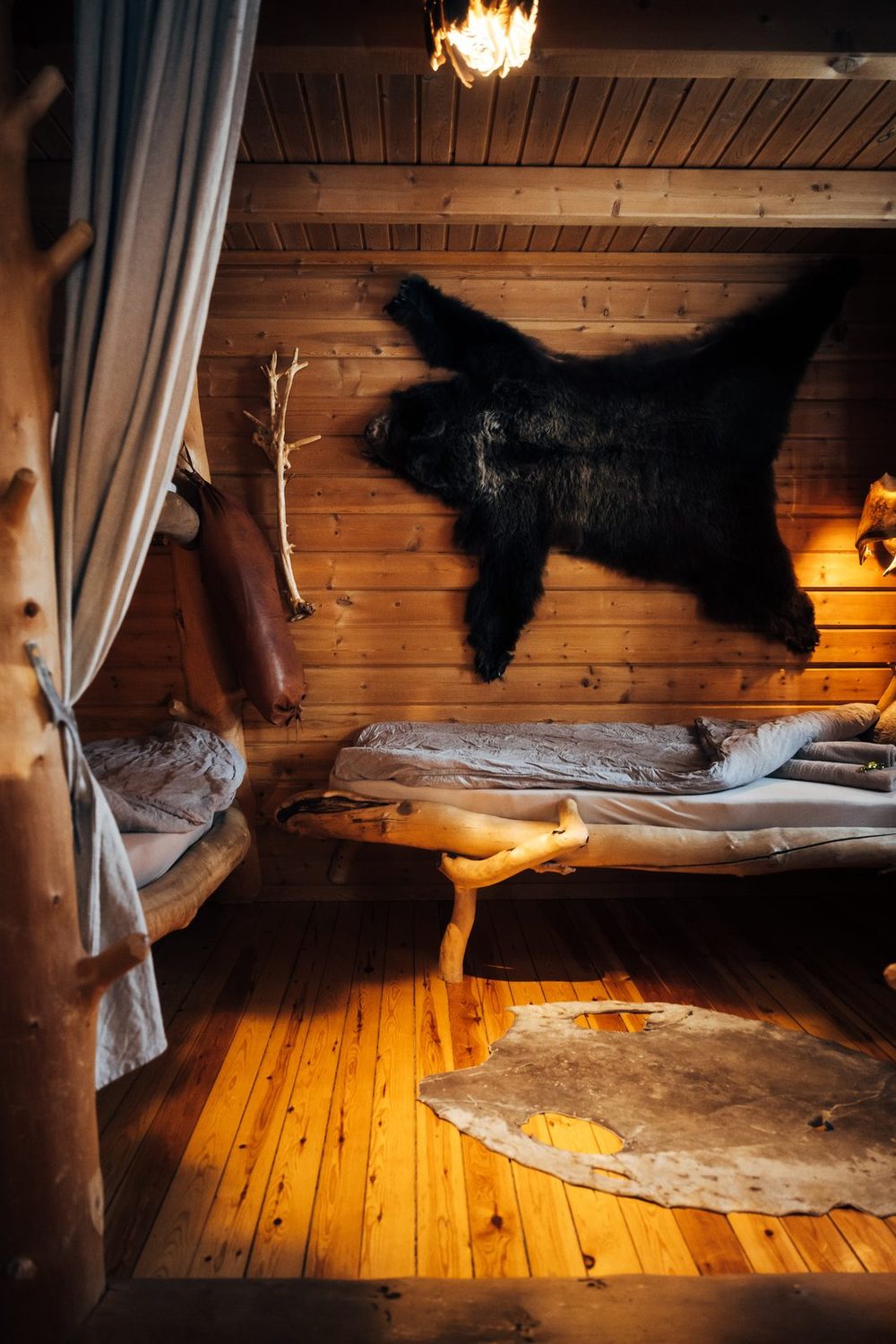 The bed under a dark hide on the log wall, the stove beside it
