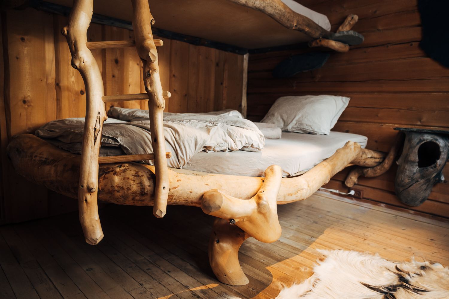 A bed built from driftwood and birch, white linen, reindeer hide on the floor
