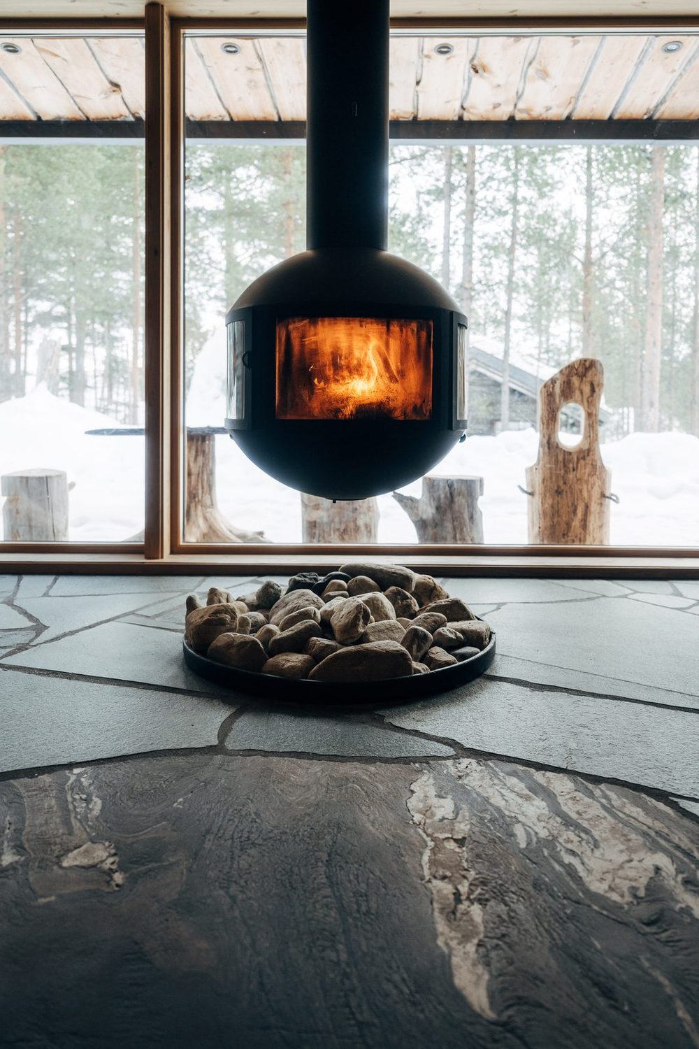 The suspended fireplace lit, the wall of glass and pines in snow behind