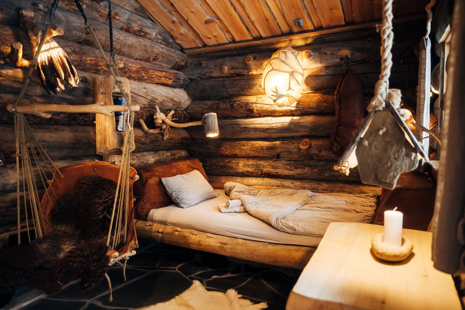 Candlelight over a low bed under log walls and hanging lamps