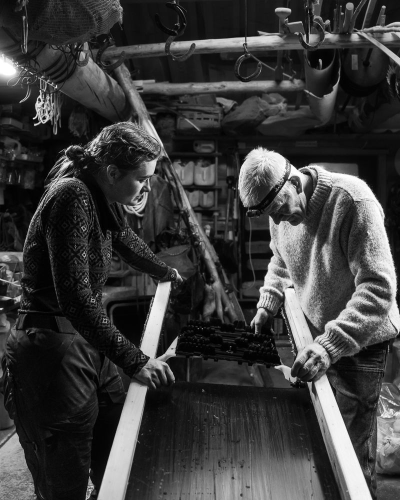 Two people shaping a long plank in the workshop, black and white