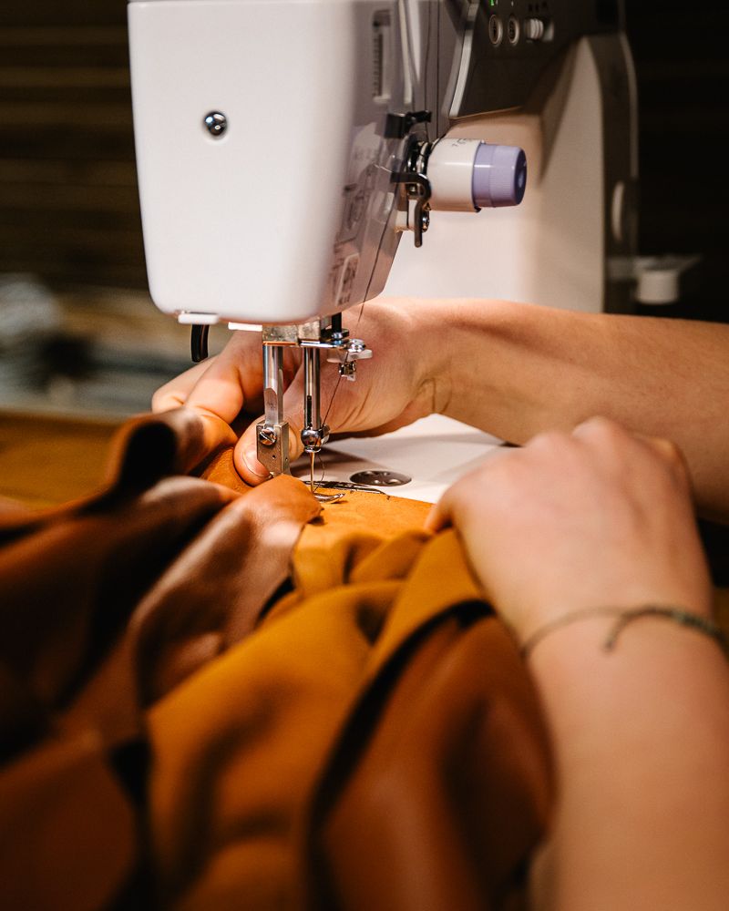 Hands guiding tan leather under a sewing machine