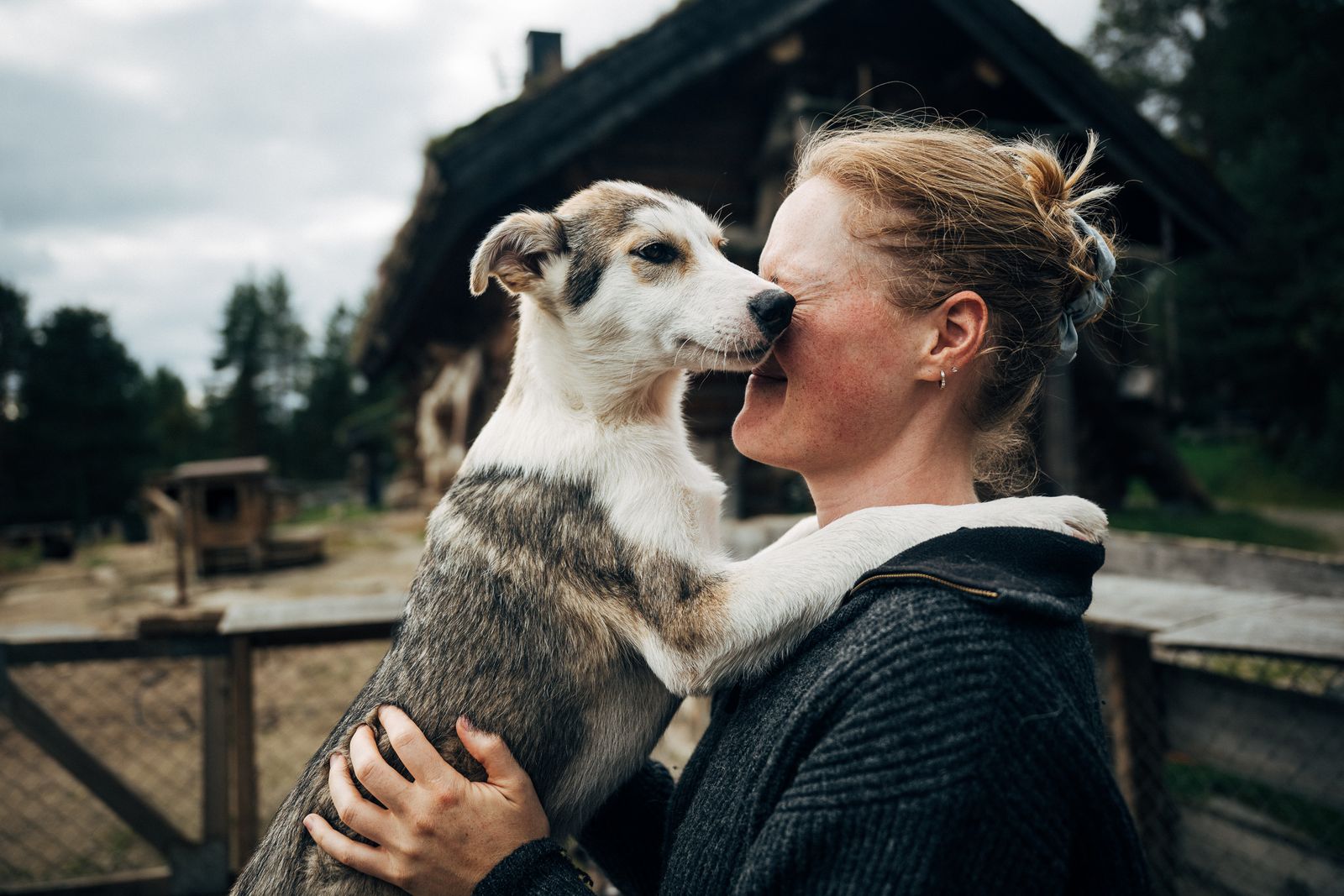 A woman holding a young husky up to her face, nose to nose, in the dog yard