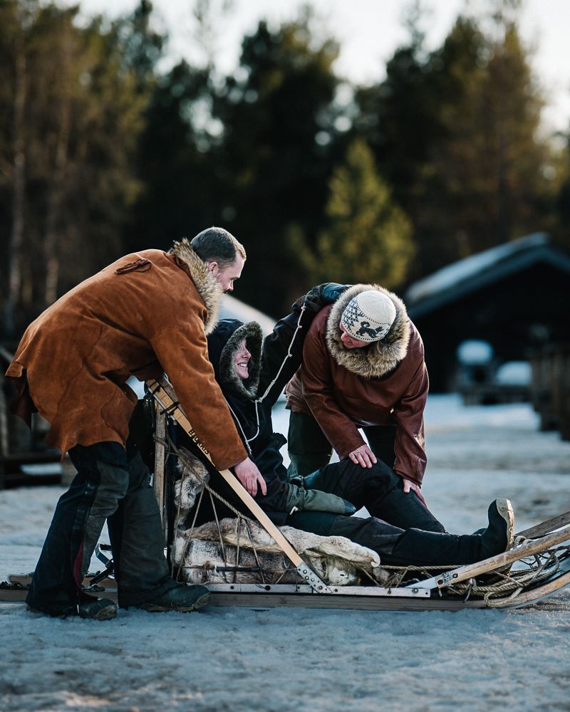 The two guides bending over the sled to tuck the passenger in