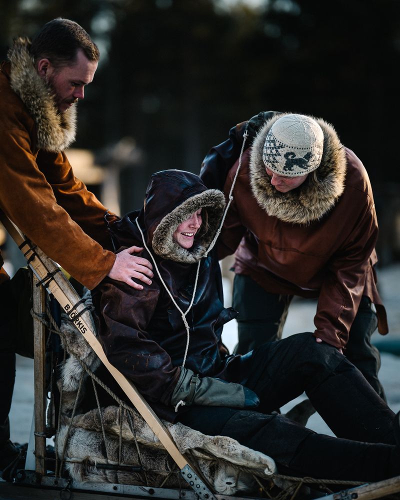 A passenger settling into the sled between two guides, a hand on each shoulder