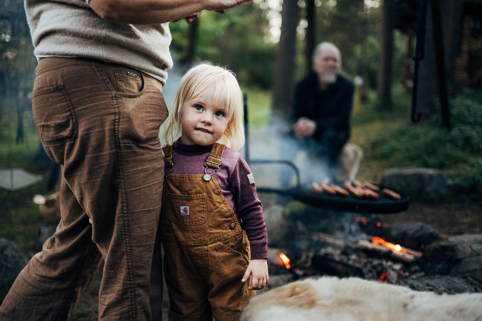 A small child in dungarees looking up, the fire and the cook behind