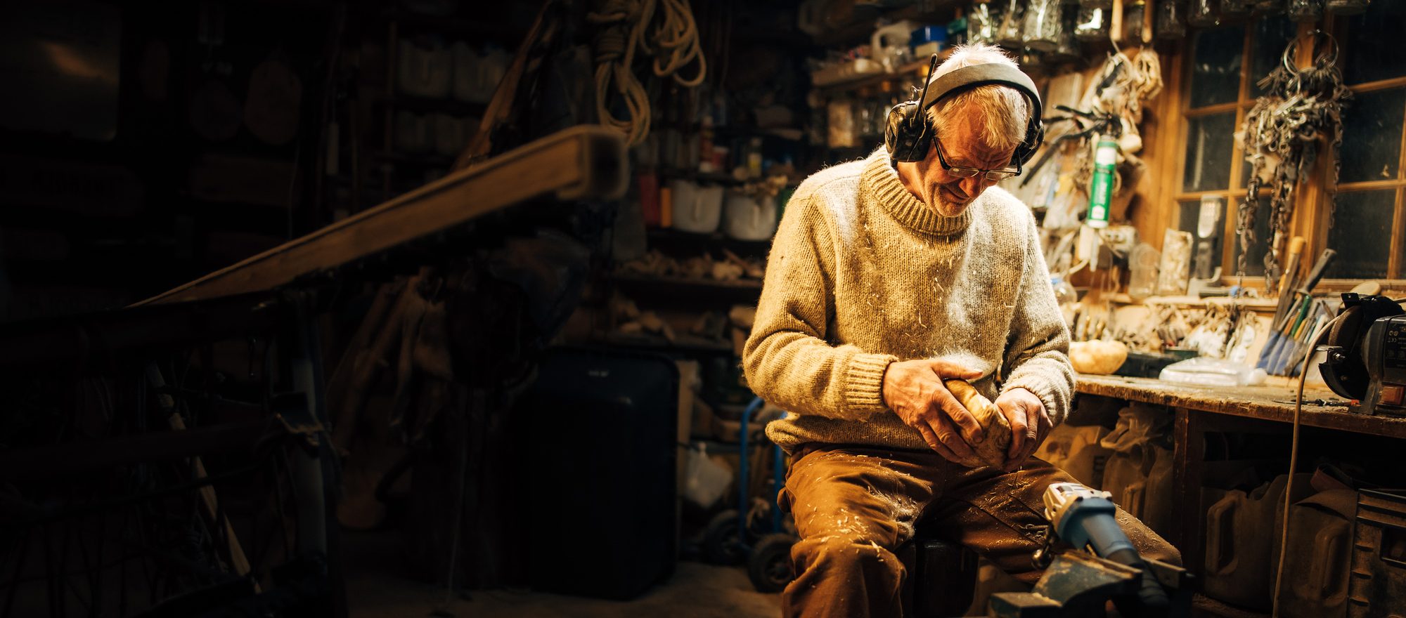 Sven in his workshop, ear defenders on, shaping a piece of birch by hand