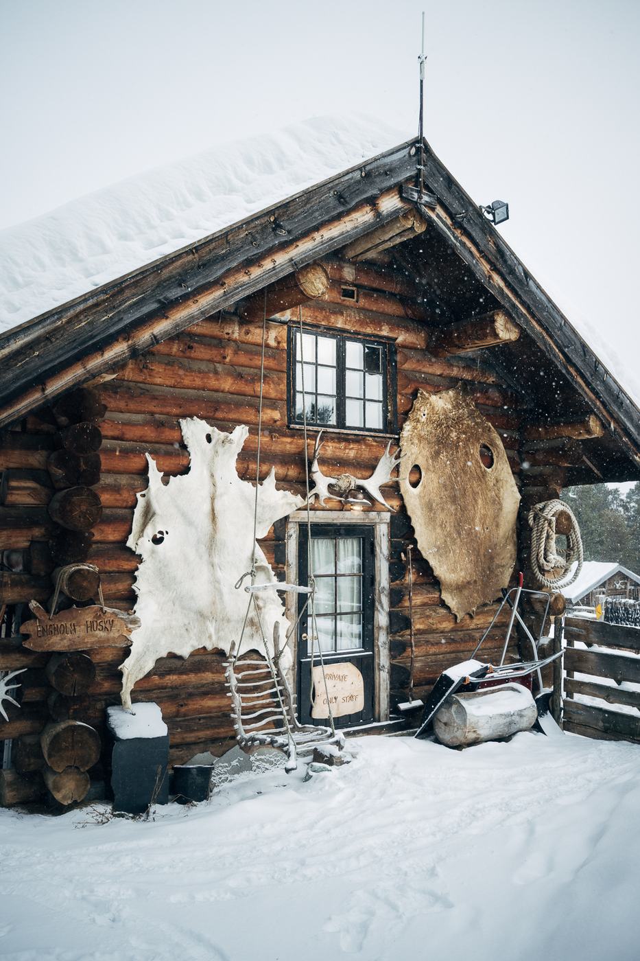 A log cabin in falling snow, reindeer hides hung by the door