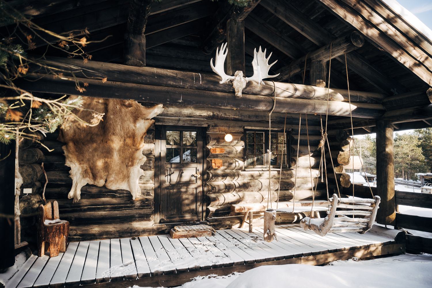 The porch under moose antlers, hides and a sled against the wall