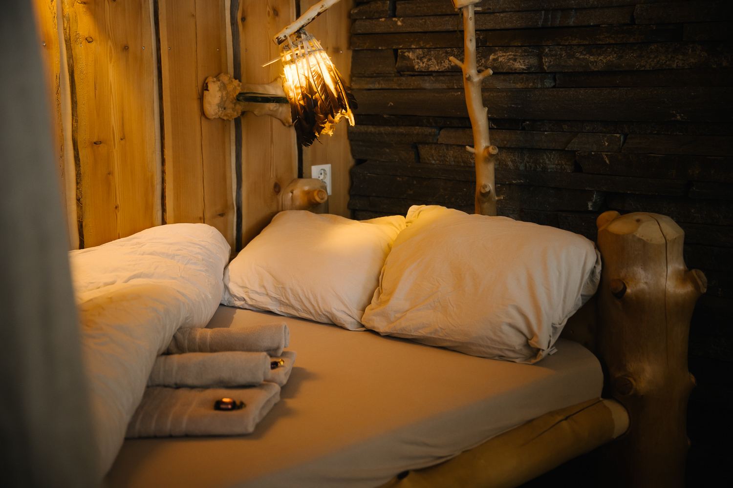 Bed with white linen under a warm lamp against log walls