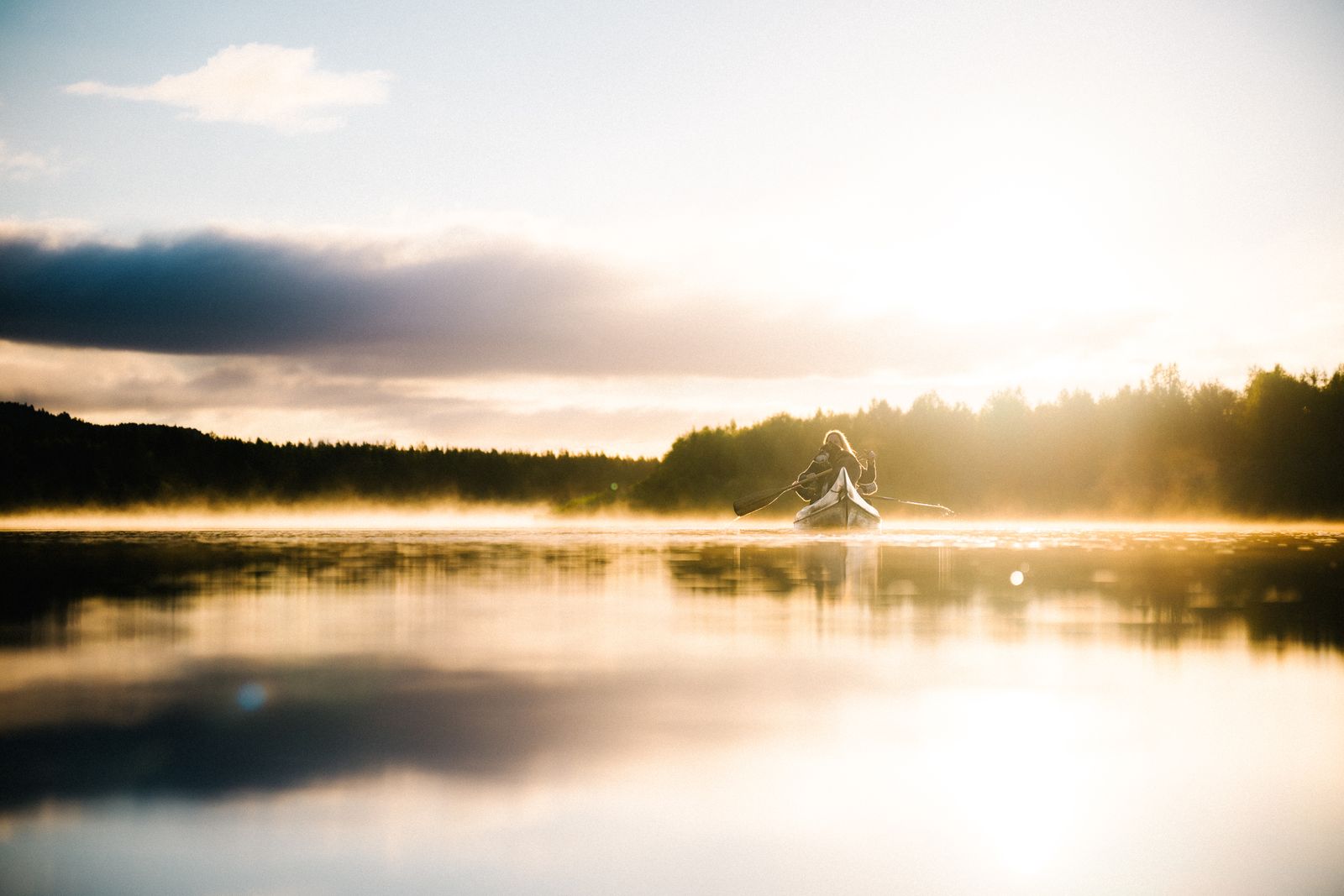 A lone canoe on the still river at sunrise, mist on the water